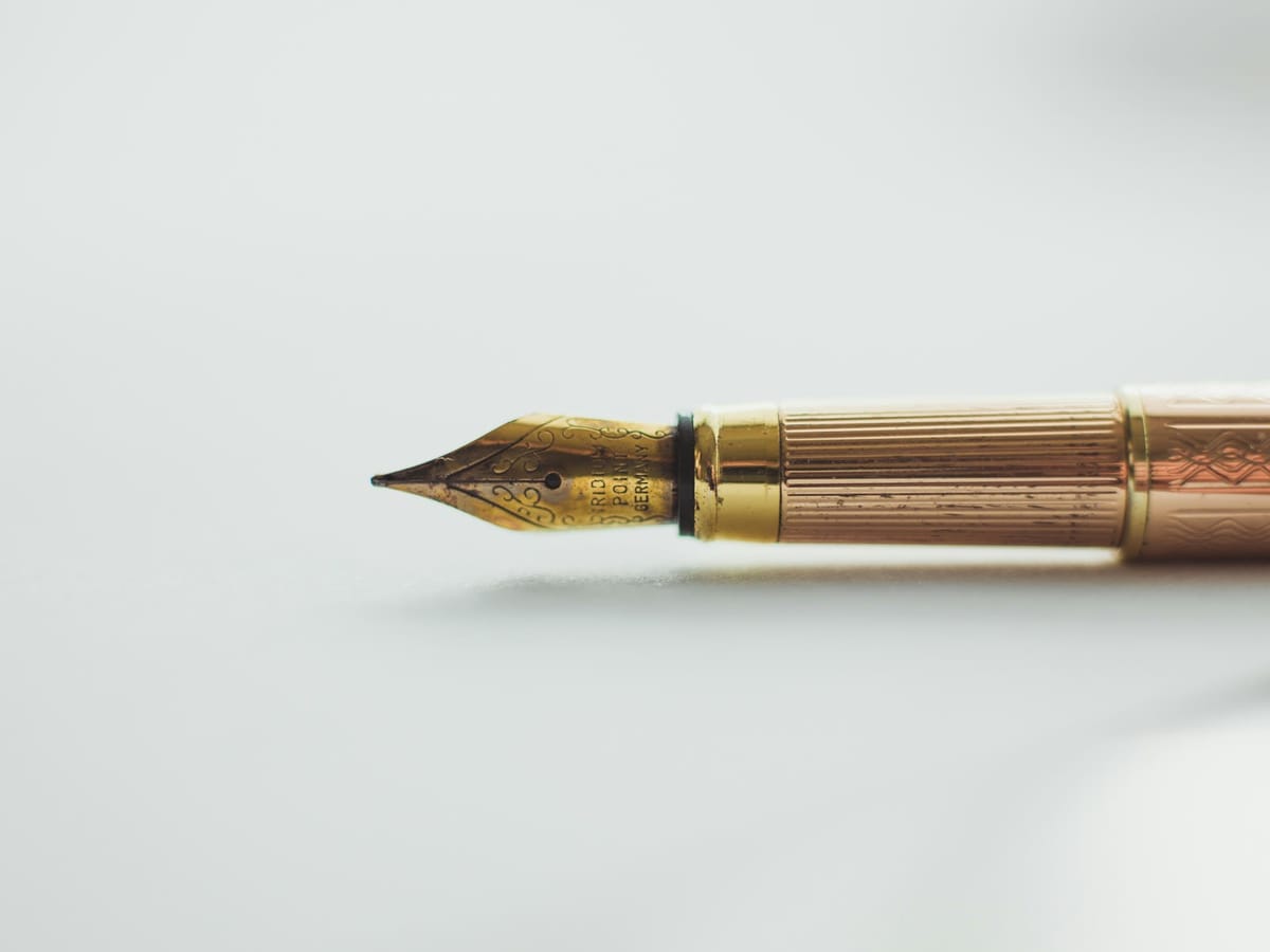 Brass quill pen on a writing surface, framing the formal Handover that closes every engineering engagement