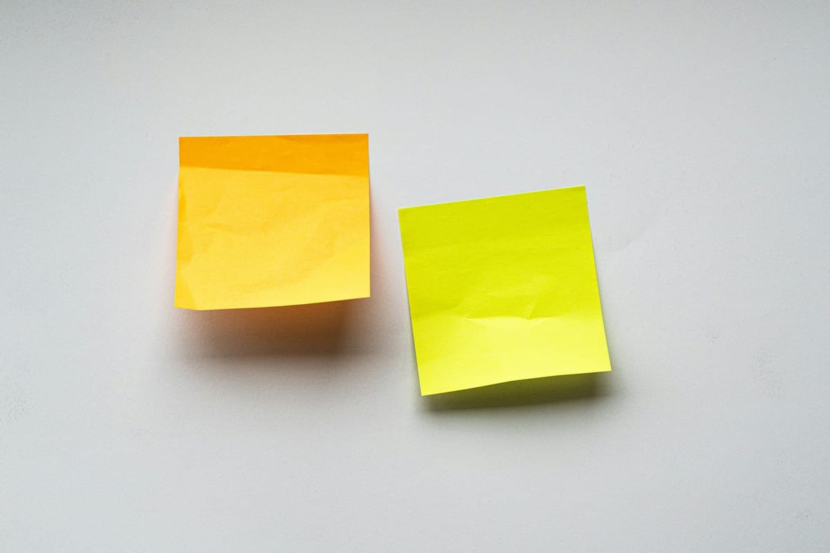 Two yellow sticky notes on a clean white wall, the visual metaphor for ongoing Retainer cadence and weekly outputs